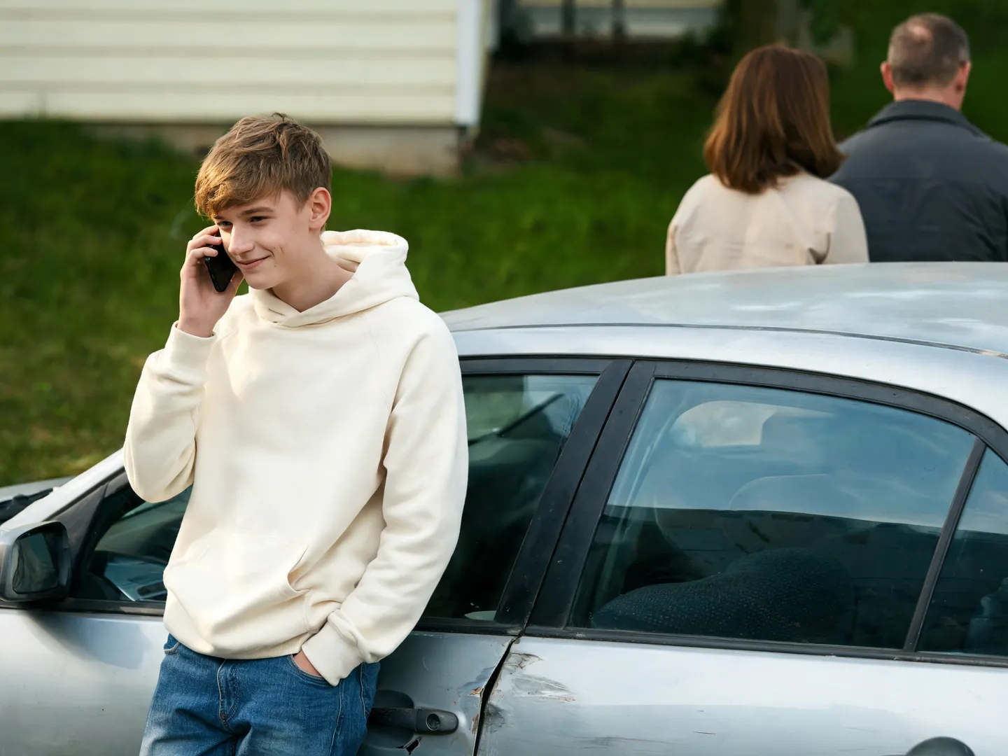 Eine junge Person telefoniert lächelnd neben einem älteren Auto.